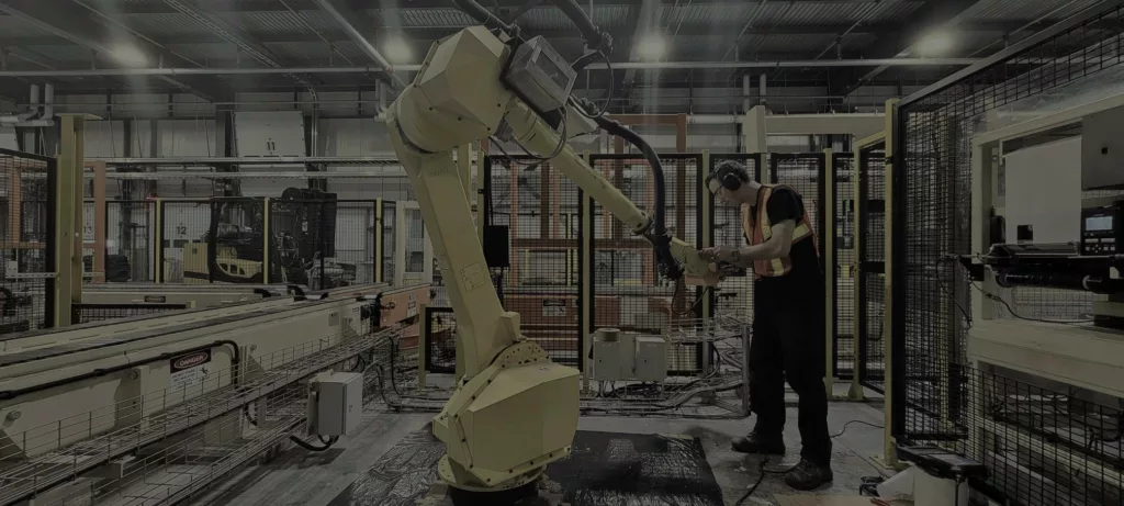 Technician standing next to a yellow industrial robot on a production line